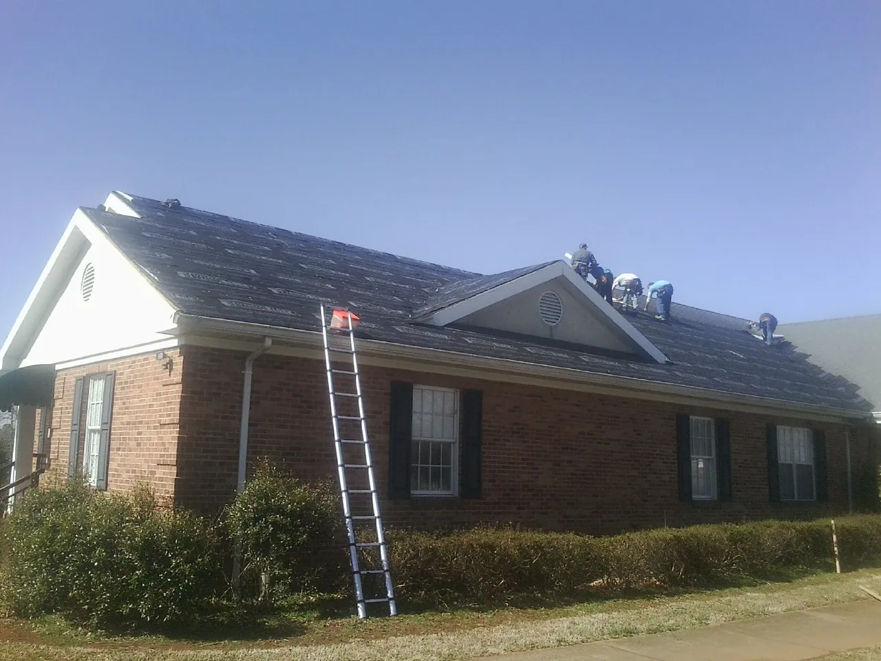 Crew tearing shingles off a brick ranch roof with a ladder set — Metal Roof Repair work by our crew in Charlestown