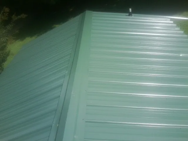 New green metal panels meeting at the ridge of a roof — Flat Roof Repair work by our crew in Charlestown