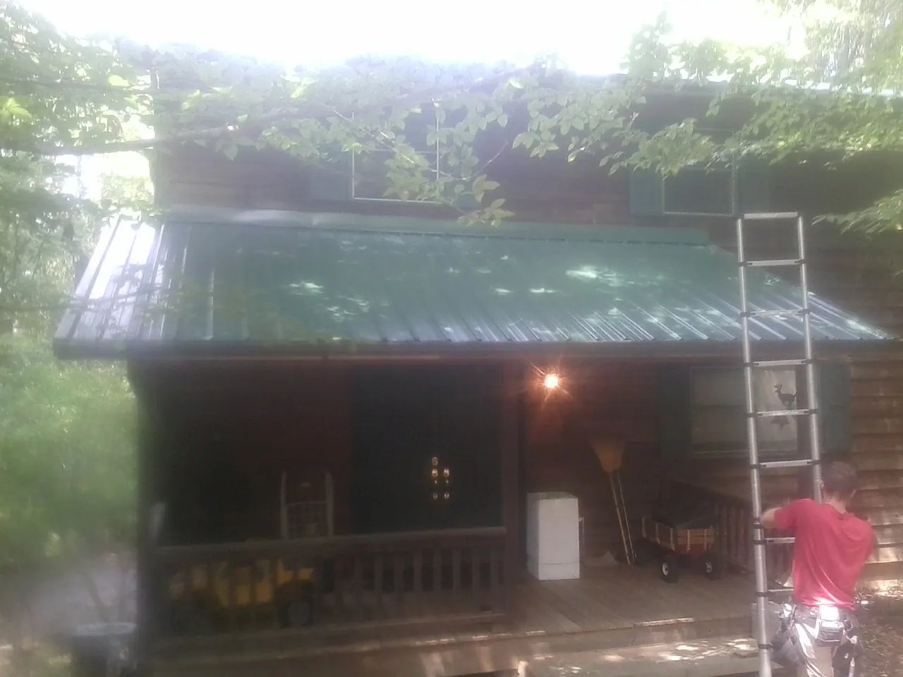 Worker on a ladder at the green porch roof of a wooded cabin in Charlestown